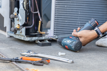 A person is fixing an air conditioner with a drill.