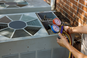 A man is working on an air conditioner outside of a brick building.