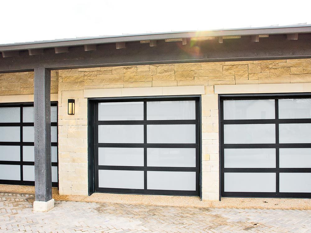 Modern garage with three frosted black-framed doors and a tan stone exterior