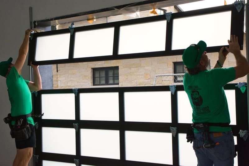 Two workers installing a large window frame with white panels inside a building opening