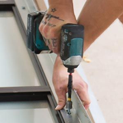 A person uses a teal cordless drill to drive a screw into a metal frame structure.