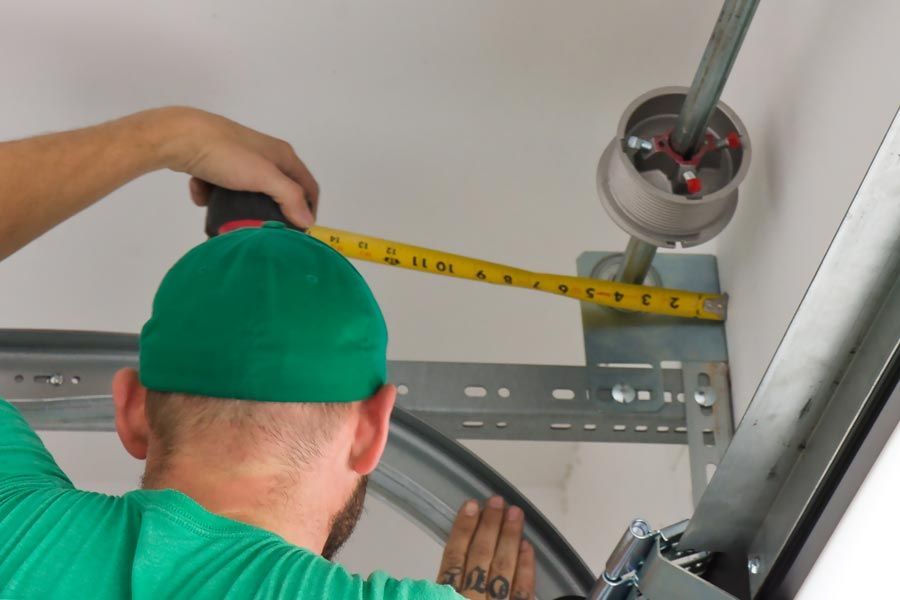 Worker in green shirt measuring a metal frame with a tape measure near a ceiling opening