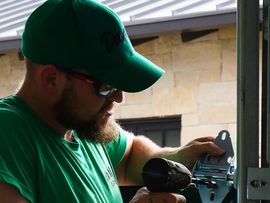 Man in green cap and shirt adjusting a window latch or hardware outdoors