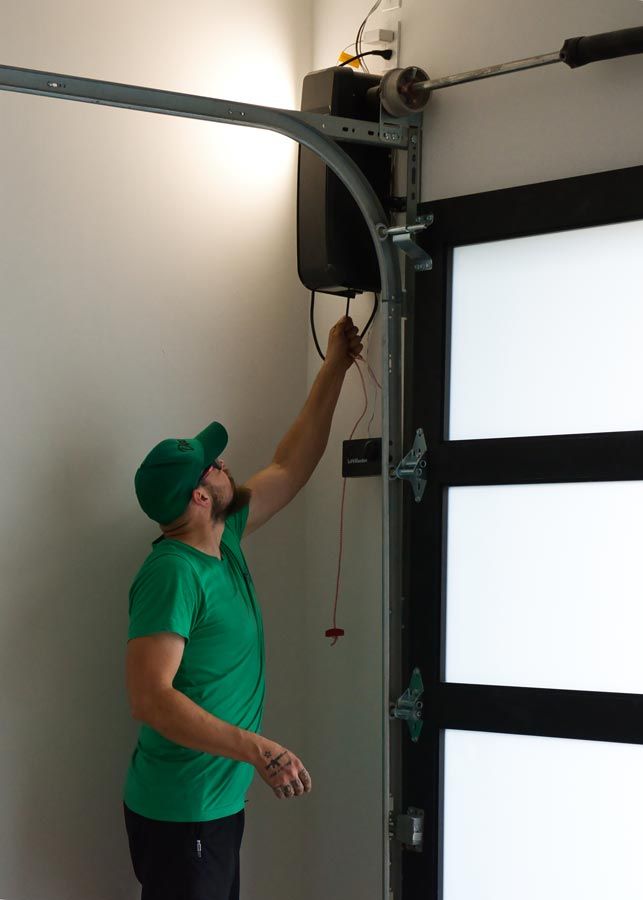 Man in green shirt adjusting a garage door opener above a white garage door