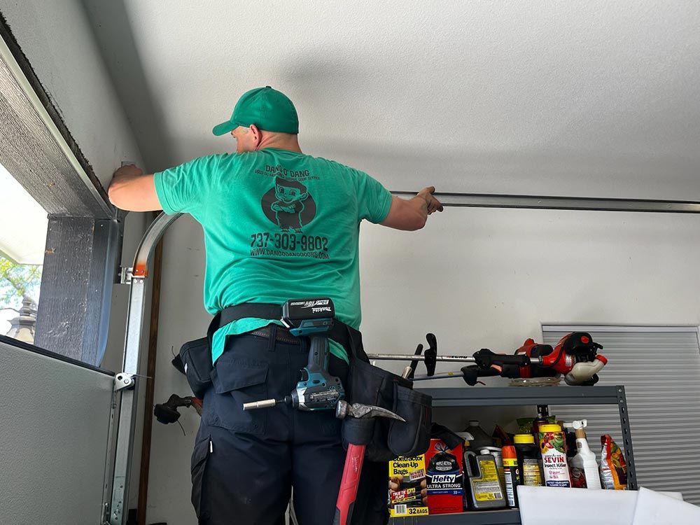 Person in green shirt adjusting a garage door opener on a ladder in a garage