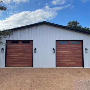 Two wood garage doors on a white metal building under a blue sky
