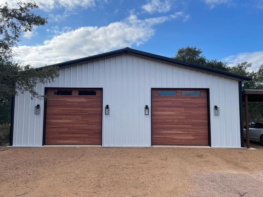 White metal garage with two wooden doors under a blue sky, set on a dirt driveway
