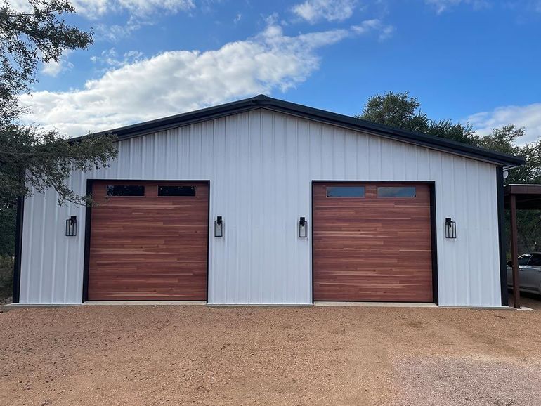 White metal garage with two wooden doors and a gravel driveway under a cloudy blue sky