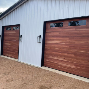 Exterior of a metal garage with two wood-paneled doors and gravel driveway