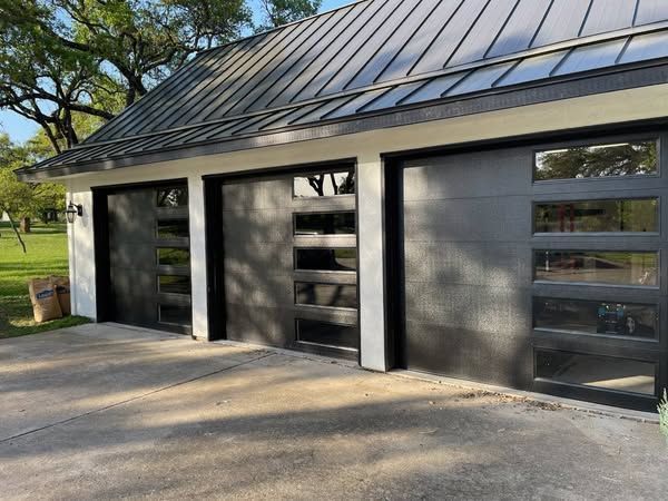 Three-car garage with black metal roof, gray exterior walls, and three large doors in a driveway
