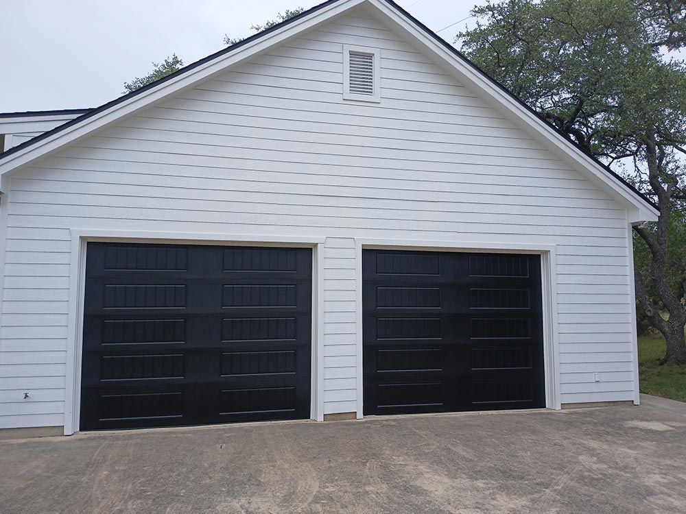 White detached garage with two black doors and a small vent under the peaked roof