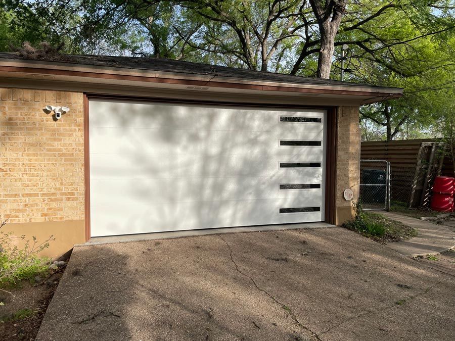White garage door on a brick house with driveway and trees overhead