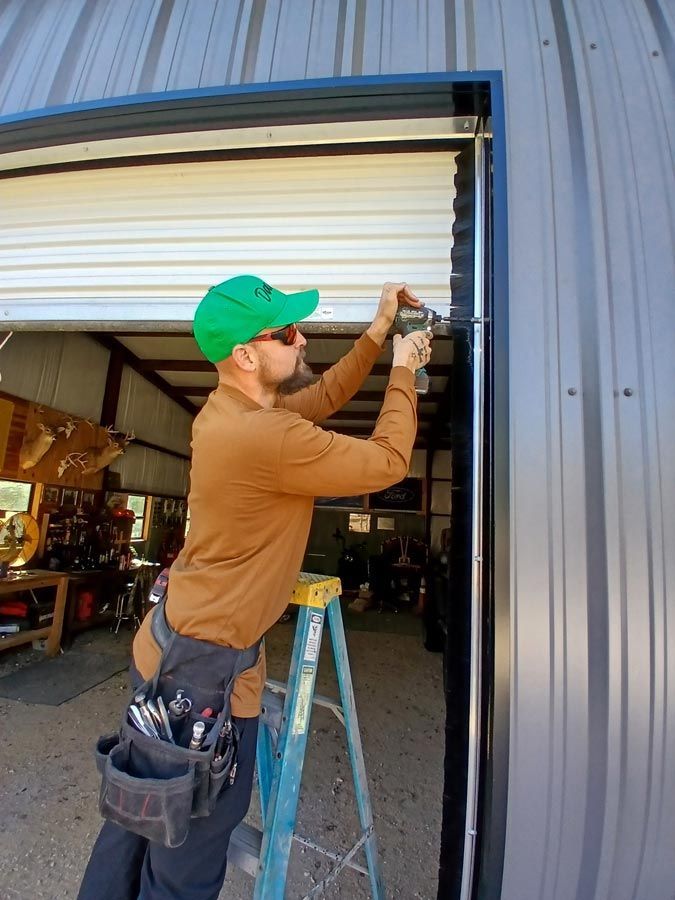 Worker using a drill to install a metal garage door frame at a workshop entrance