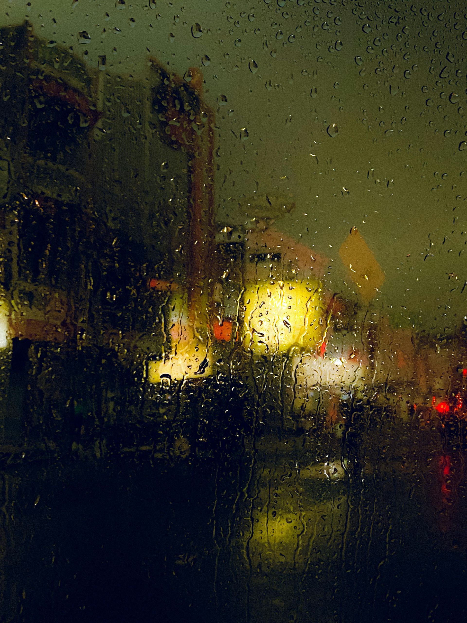 Blurry, glittering neon façades seen through a rain stained window pane.