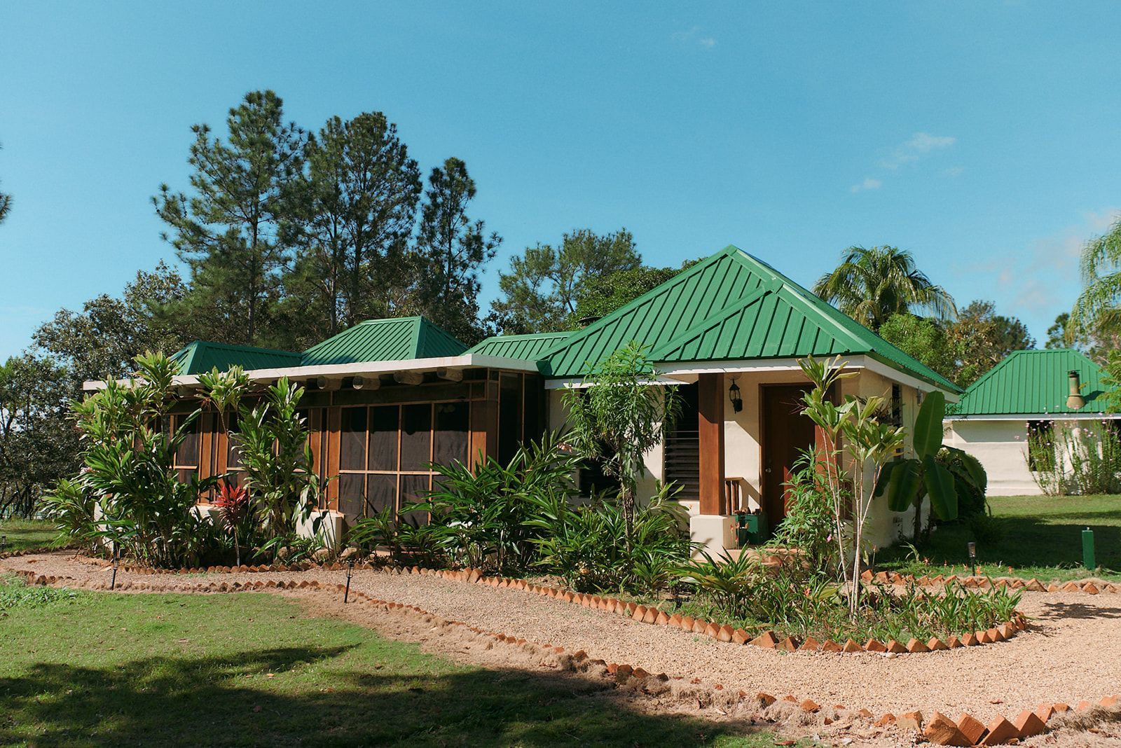 A boutique cottage with elegant green roofs, nestled in vibrant tropical landscaping and serene pathways.