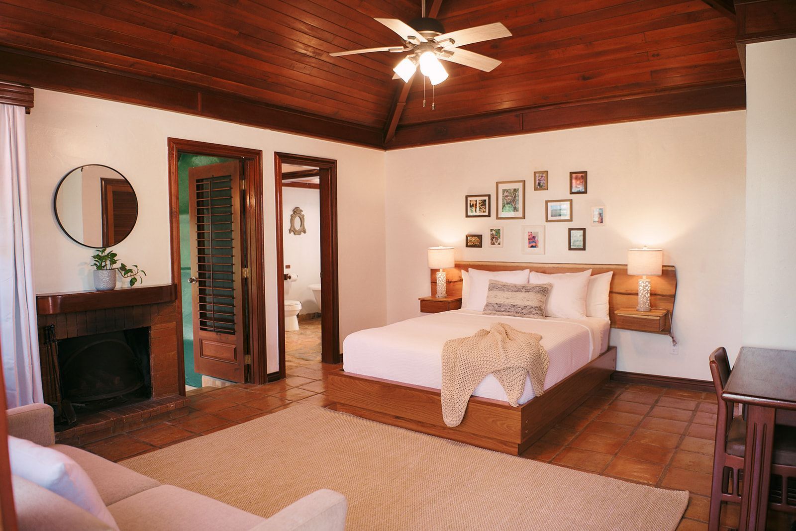 A bedroom with a king size bed , a couch , a fireplace and a ceiling fan.