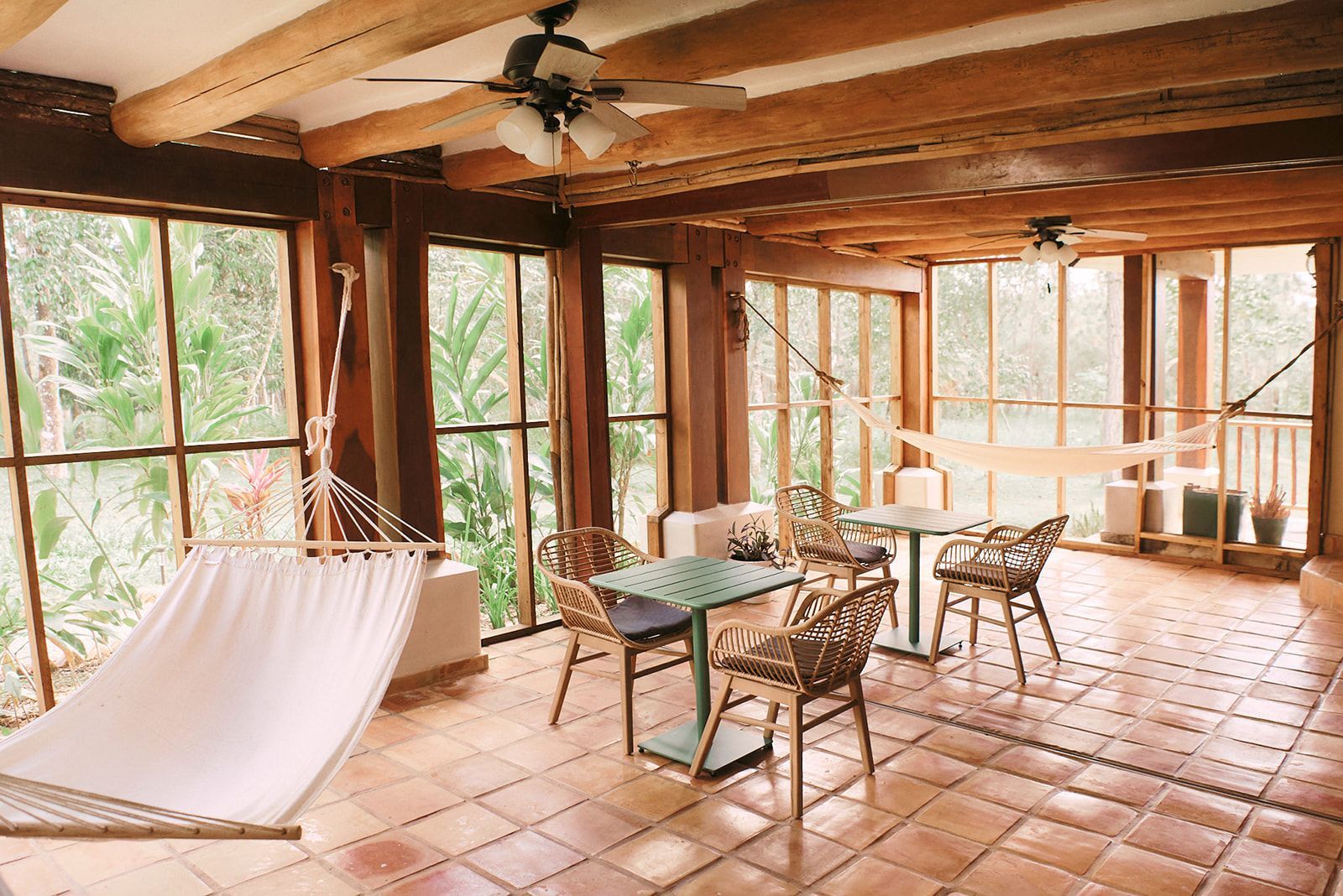 Rustic wooden beams, tile floors, hammocks, and seating areas on a screened-in porch with garden views.