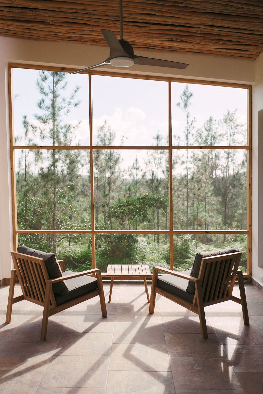 An outdoor screened-in veranda featuring cozy wooden chairs, offering serene views of the expansive pine forest reserve.