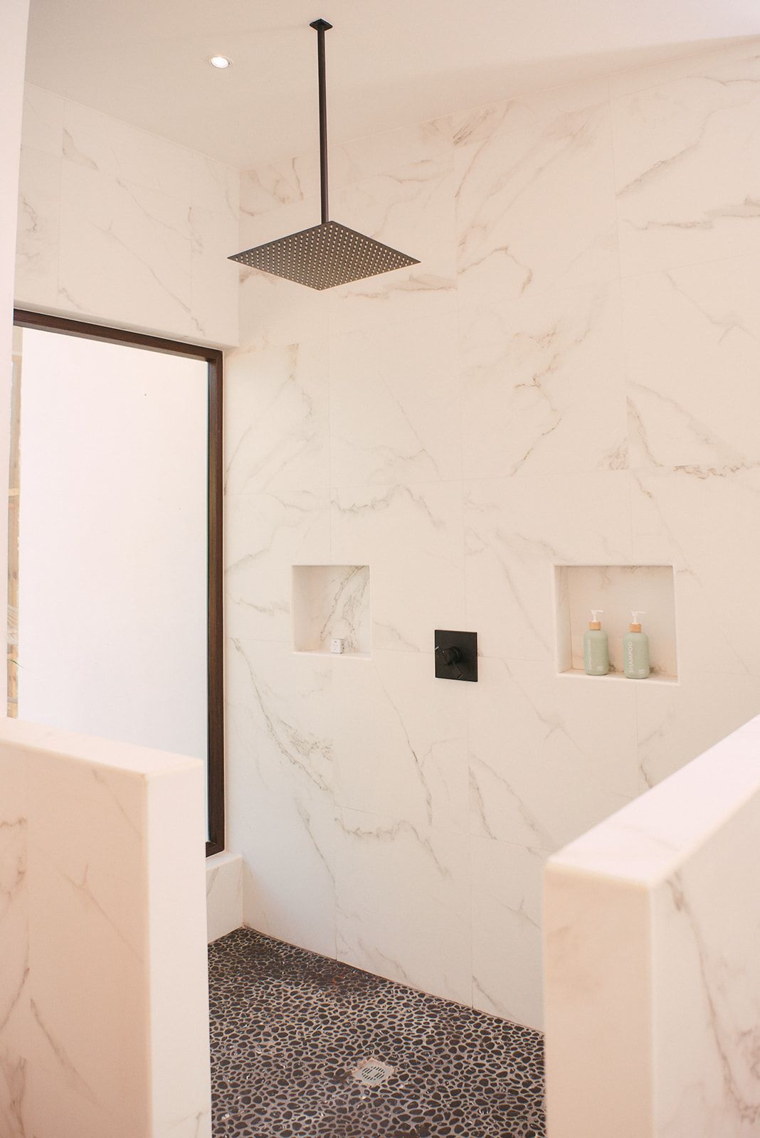 A modern, open-concept shower in the Valley View Villas featuring a rainfall showerhead, marble walls