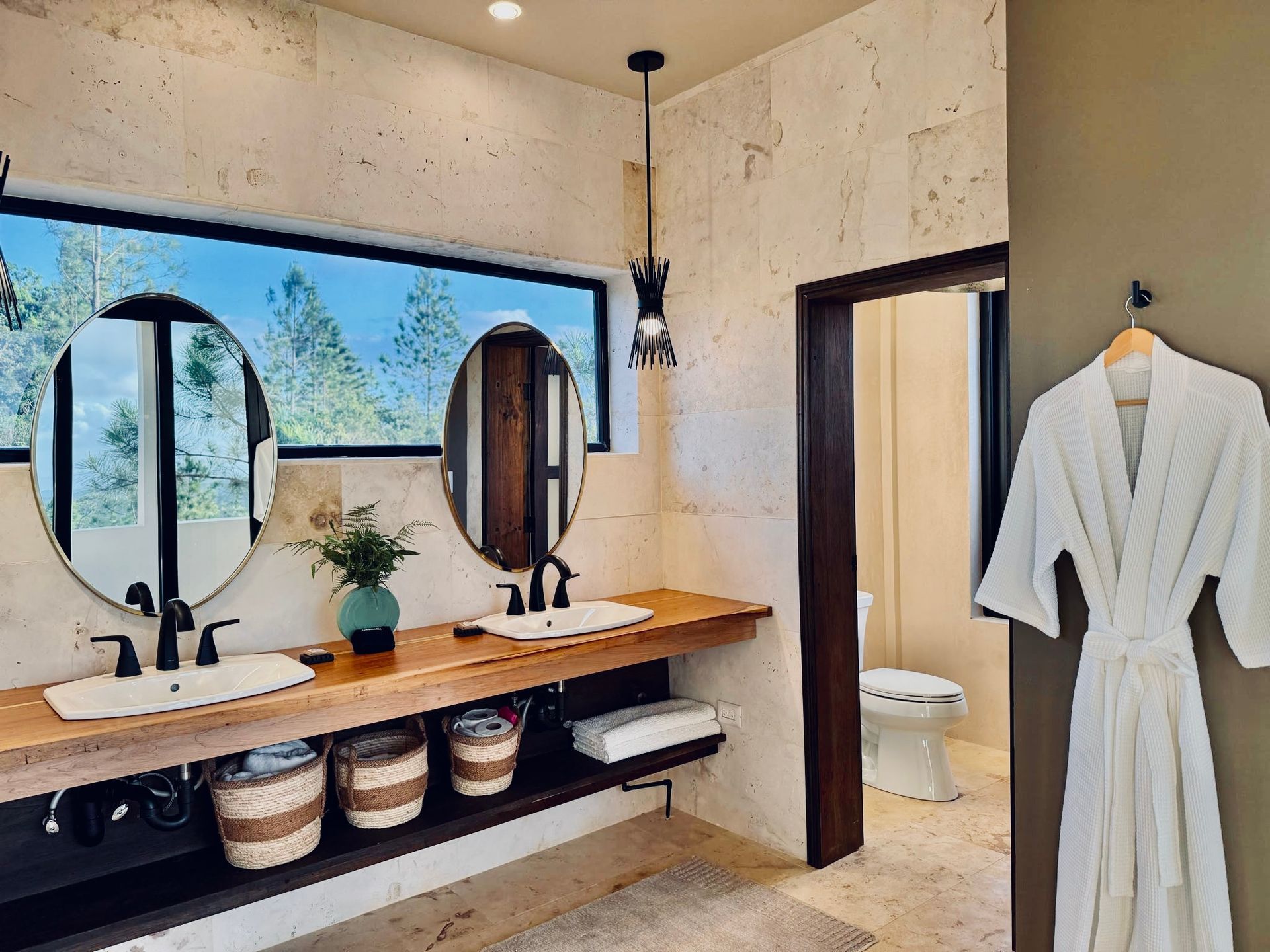A bathroom with two sinks , two mirrors and a robe hanging on the wall.
