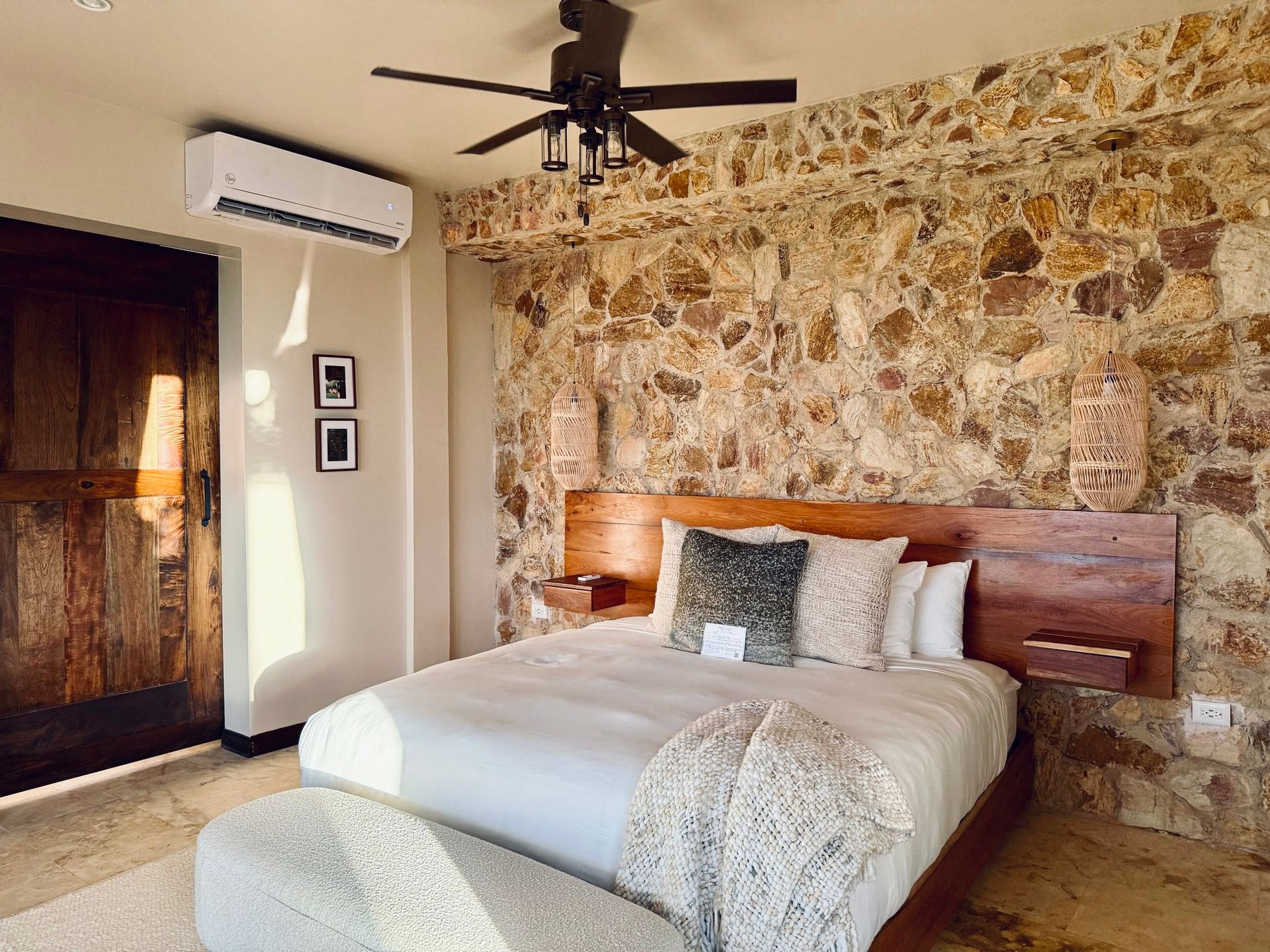 A bedroom with a bed , ceiling fan , and stone wall.