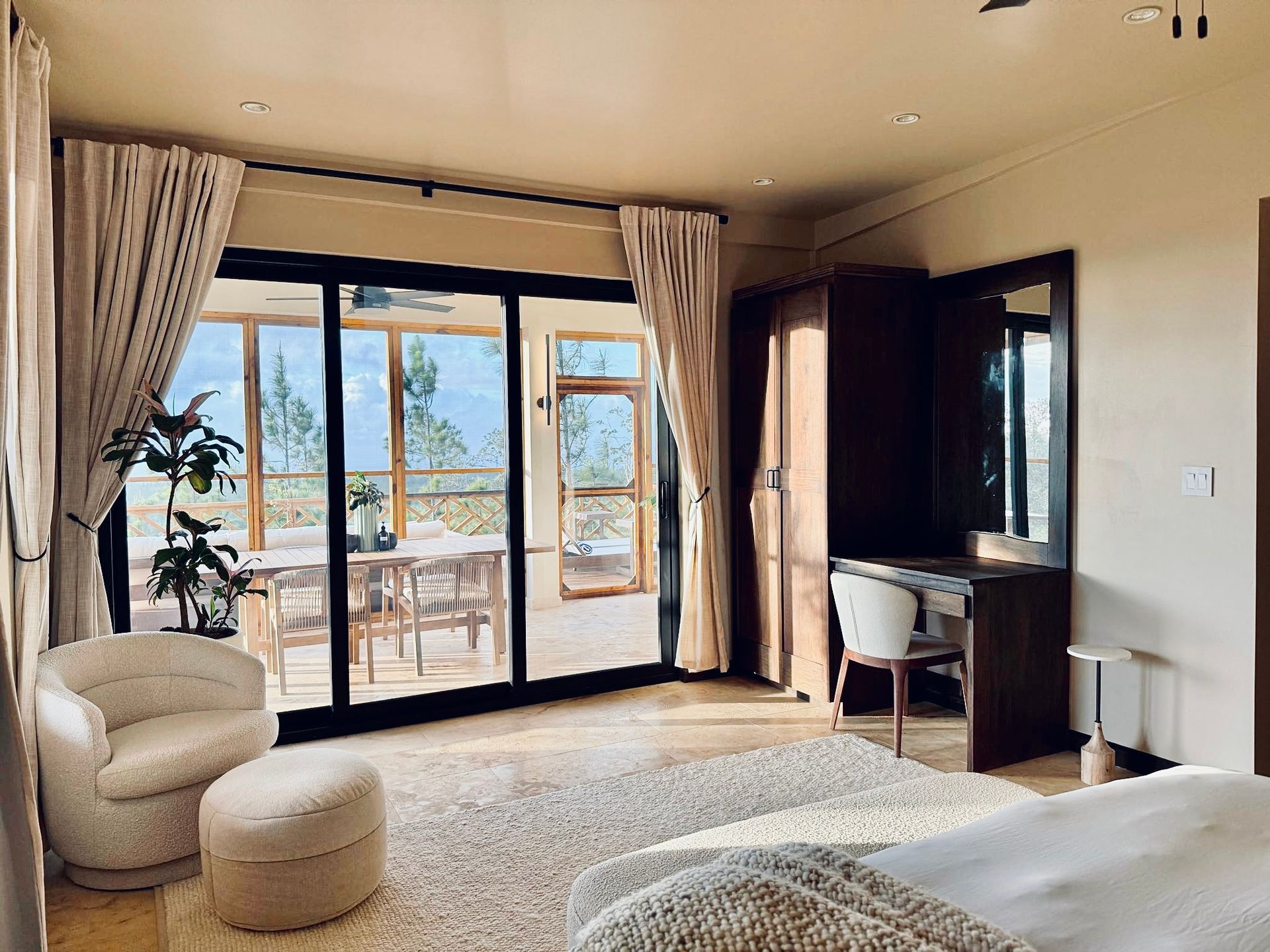 A bedroom with a large bed , chair , ottoman and sliding glass doors.