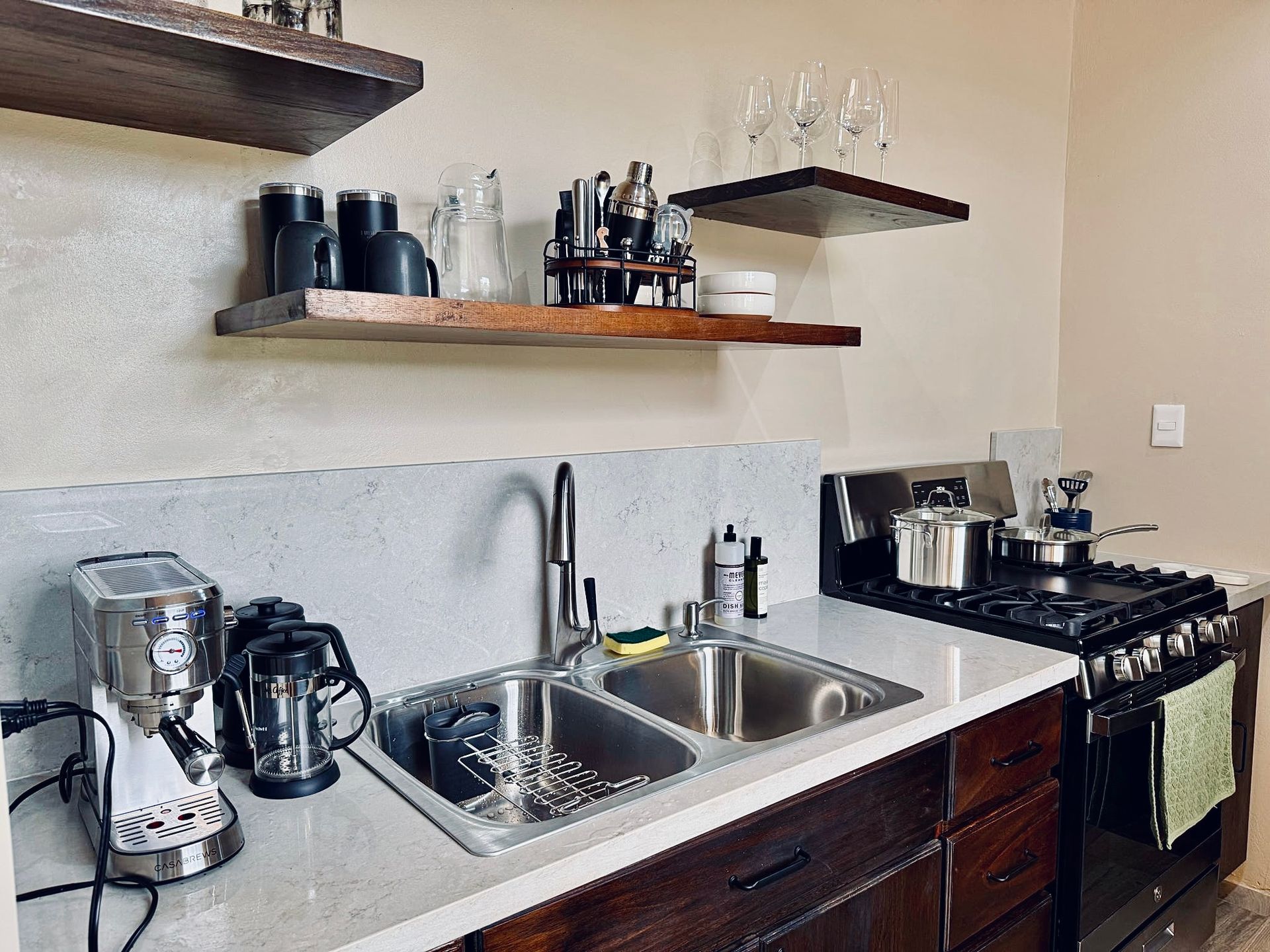 A kitchen with a sink , stove , and shelves.