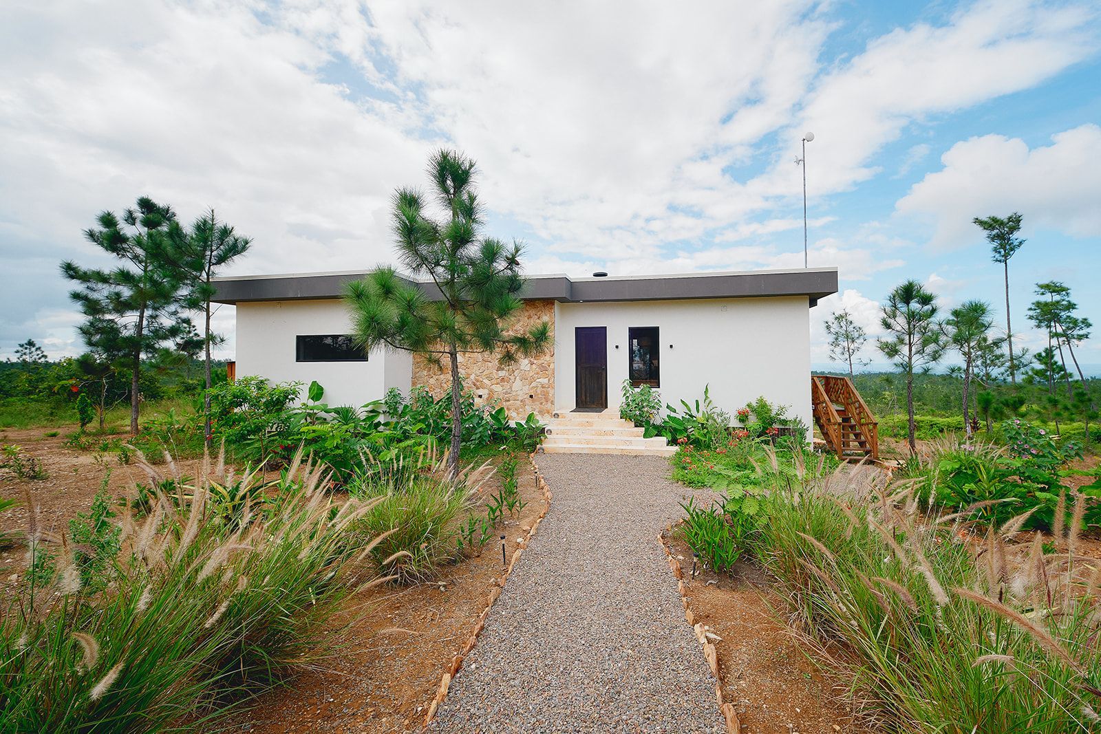 White building with rock accents, surrounded by greenery and a gravel path leading to the entrance.
