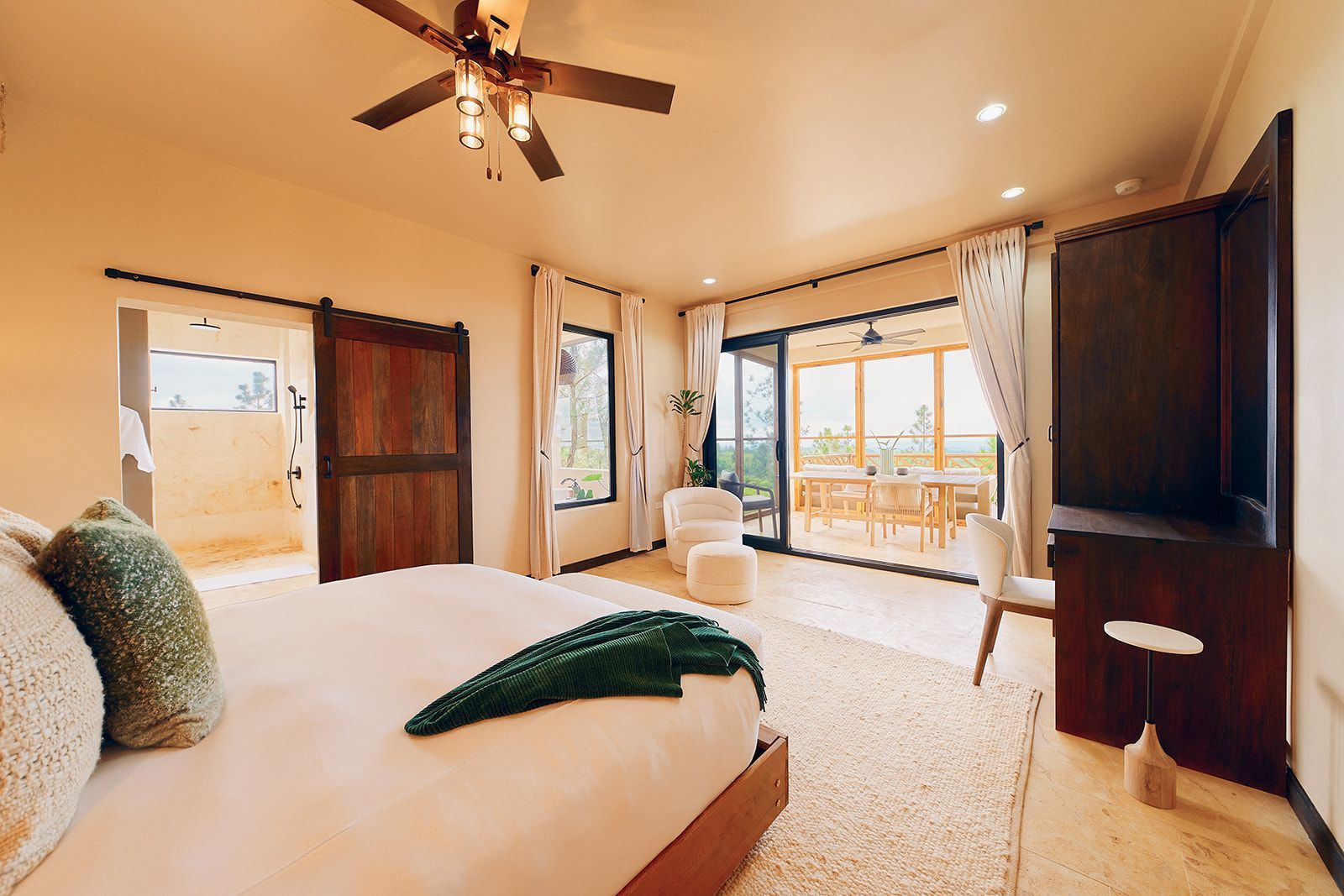 Bedroom with king bed, open to a balcony. Sliding barn door to the bathroom. Neutral color palette, ceiling fan.