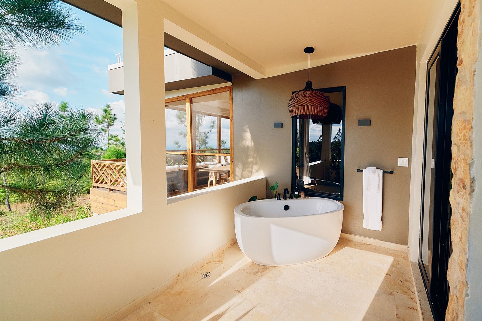 Outdoor bathroom with white tub, hanging light, and views.
