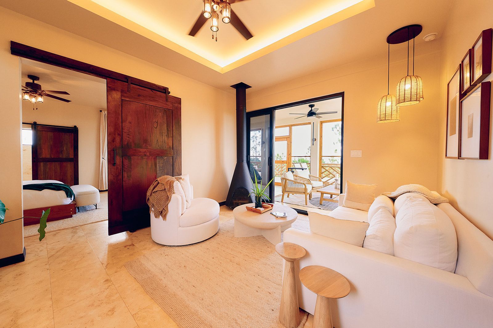 Cozy living room with open sliding door to balcony, white furniture, rustic barn door, fireplace, and pendant lights.