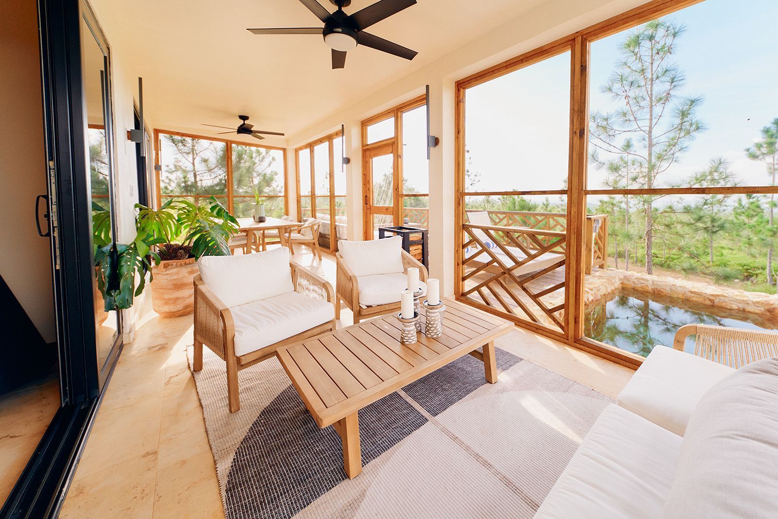 A sunroom with wooden furniture, large windows overlooking a forest and small pool.