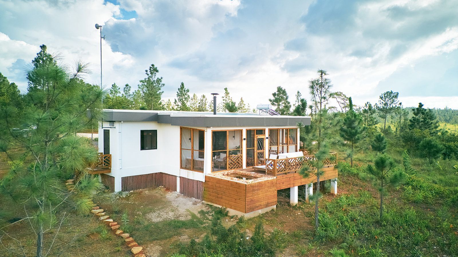 White cabin with wood accents and deck in a wooded area, under a cloudy sky.