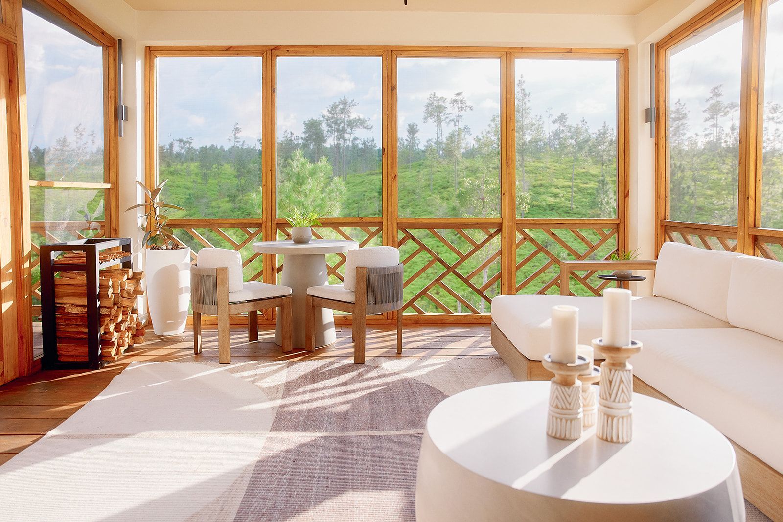 Sunroom with white furniture, wooden frames and a view of green trees outside.