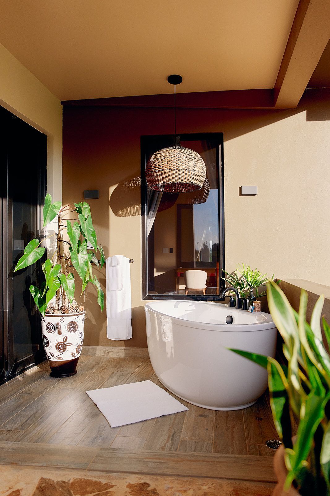 Outdoor bathroom with a white tub, plants, and a woven light fixture.