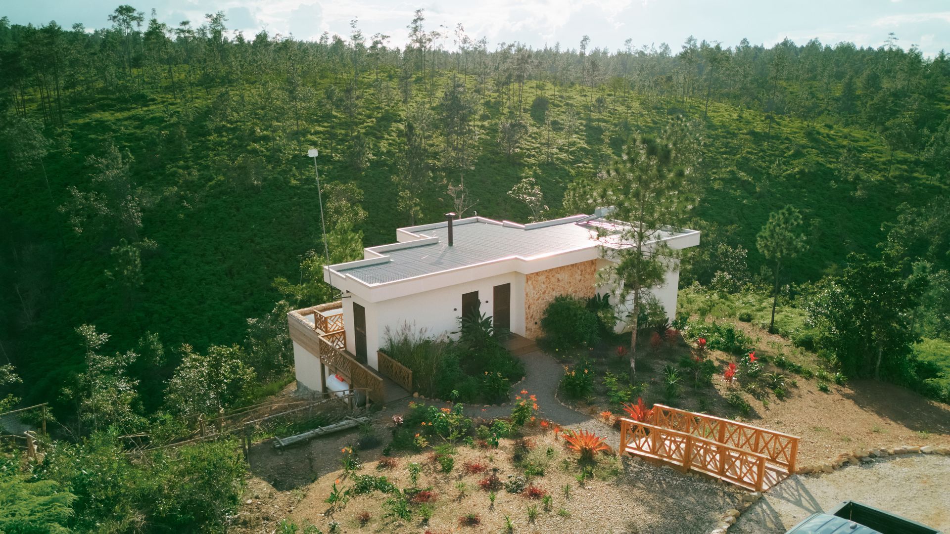 White building nestled in lush green trees with wooden bridge.