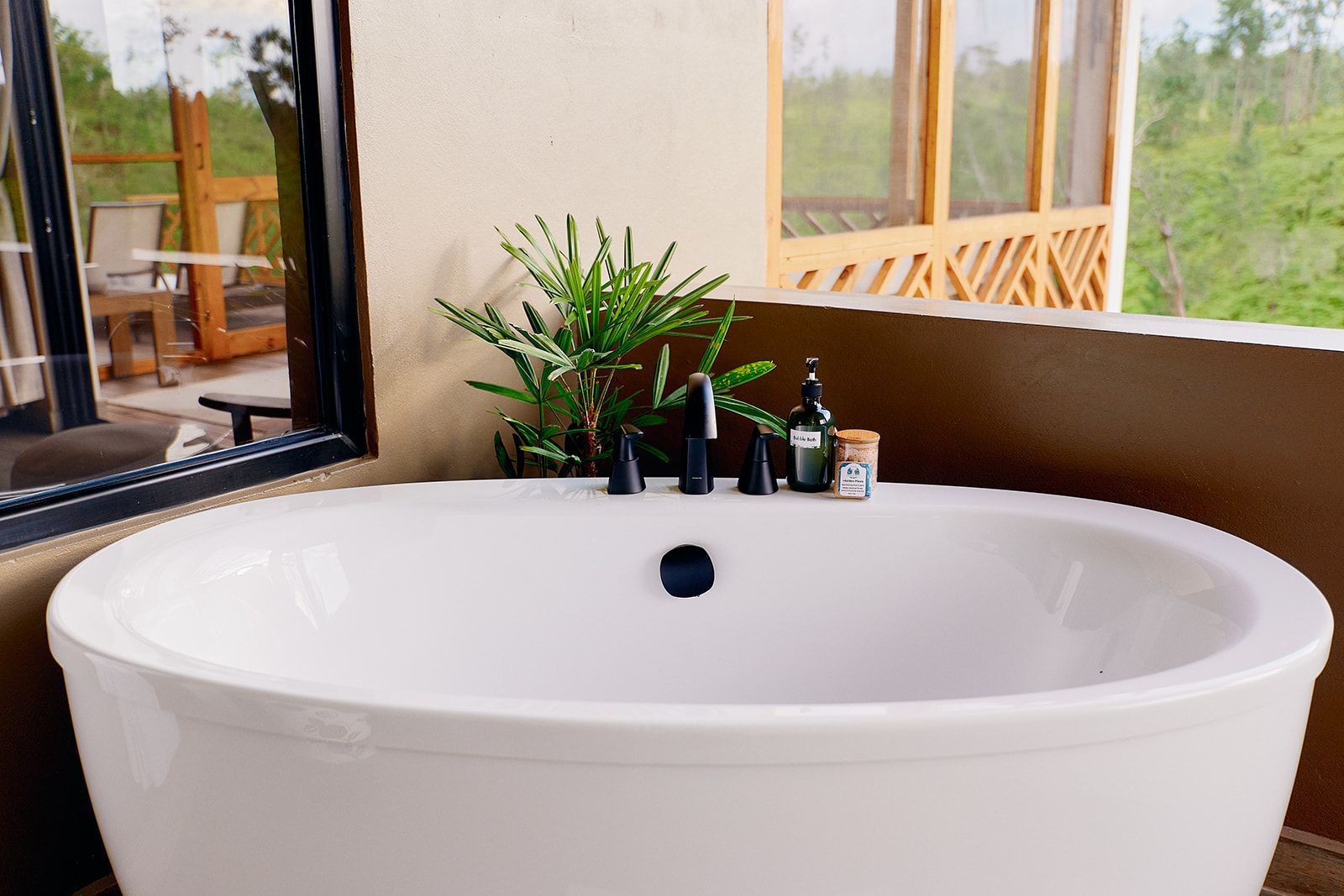 White bathtub on a balcony, with plants and a view of green trees through a screen.