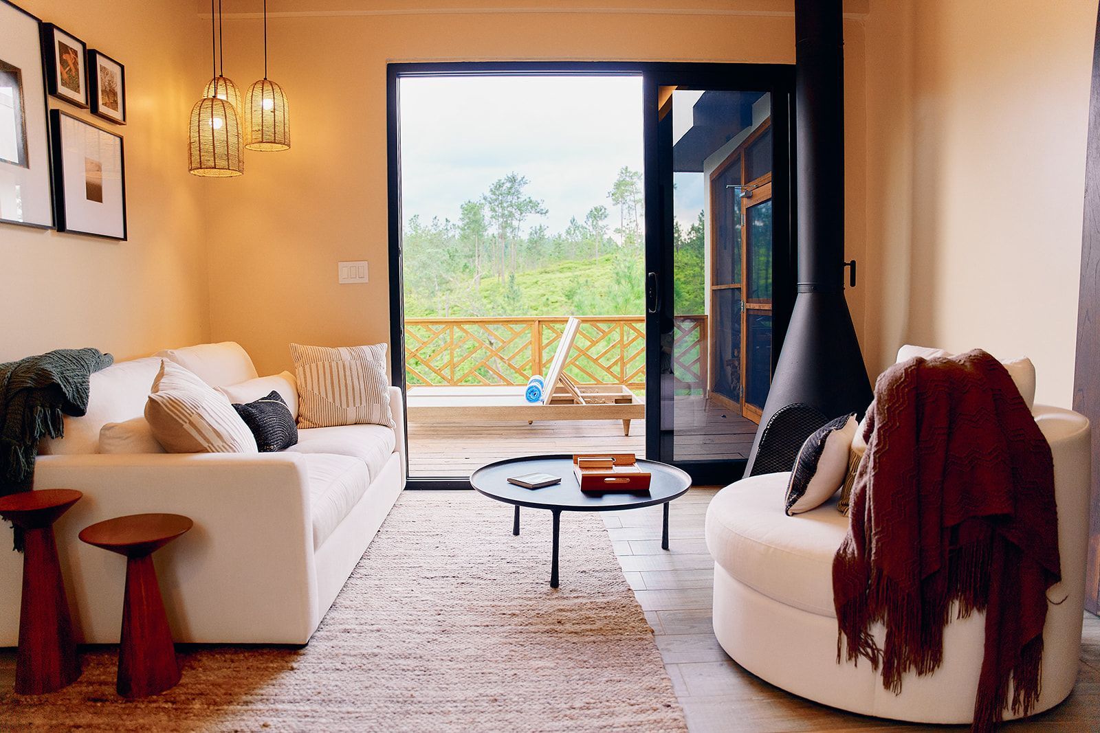 Cozy living room with a white sofa, armchair, and a dark fireplace, leading to a balcony with green scenery.