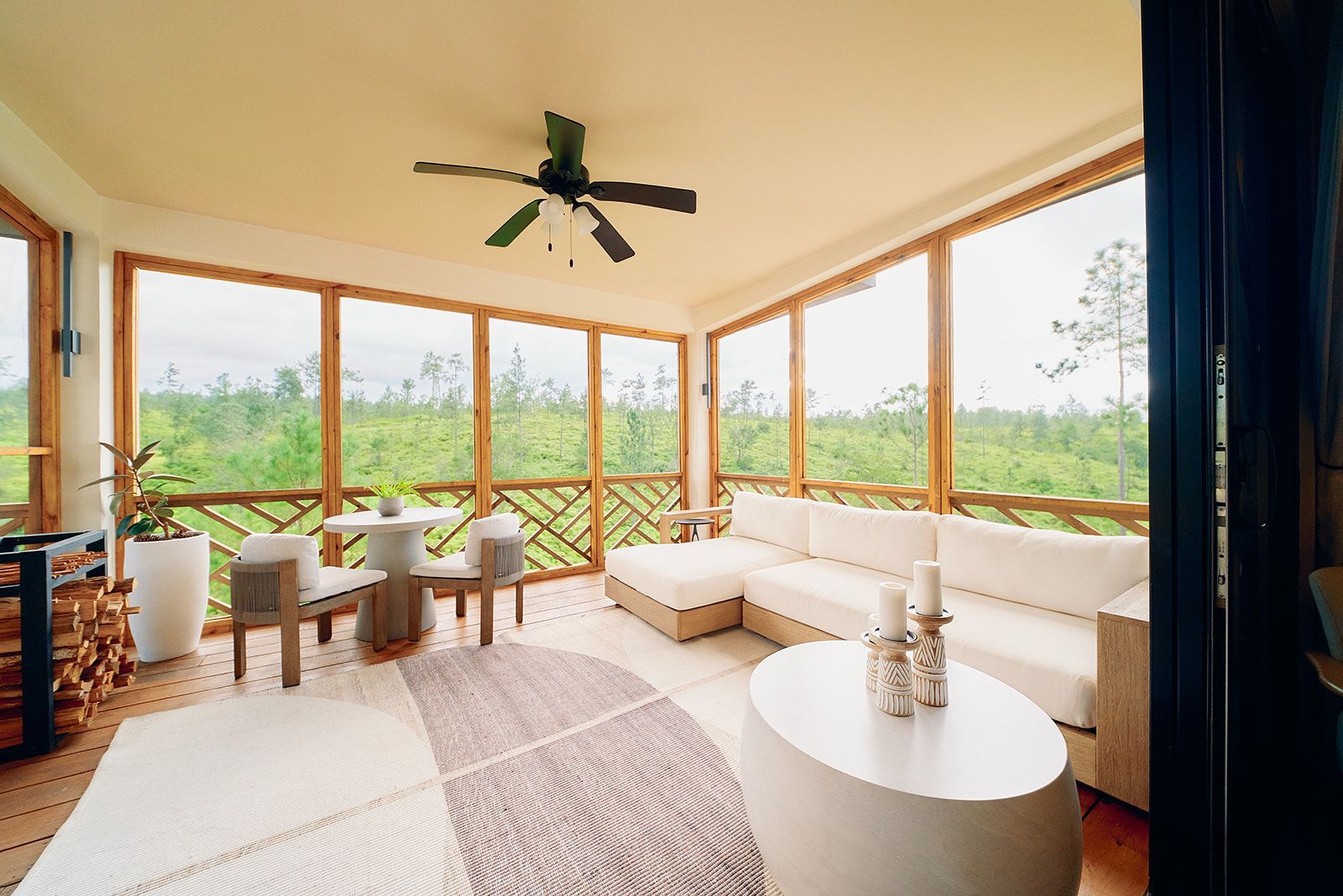 Sunroom with white sofa, chairs, and oval coffee table; screened windows overlook greenery.