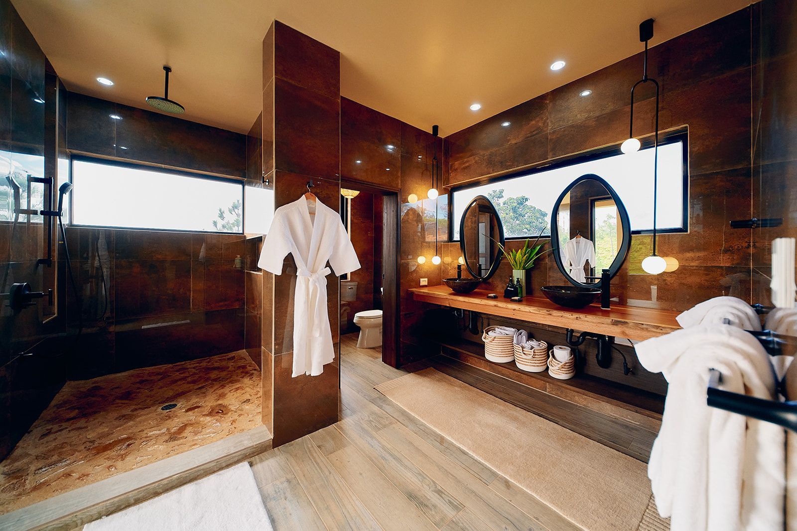 Luxurious bathroom with dark tile, large windows, double sinks, and a walk-in shower.
