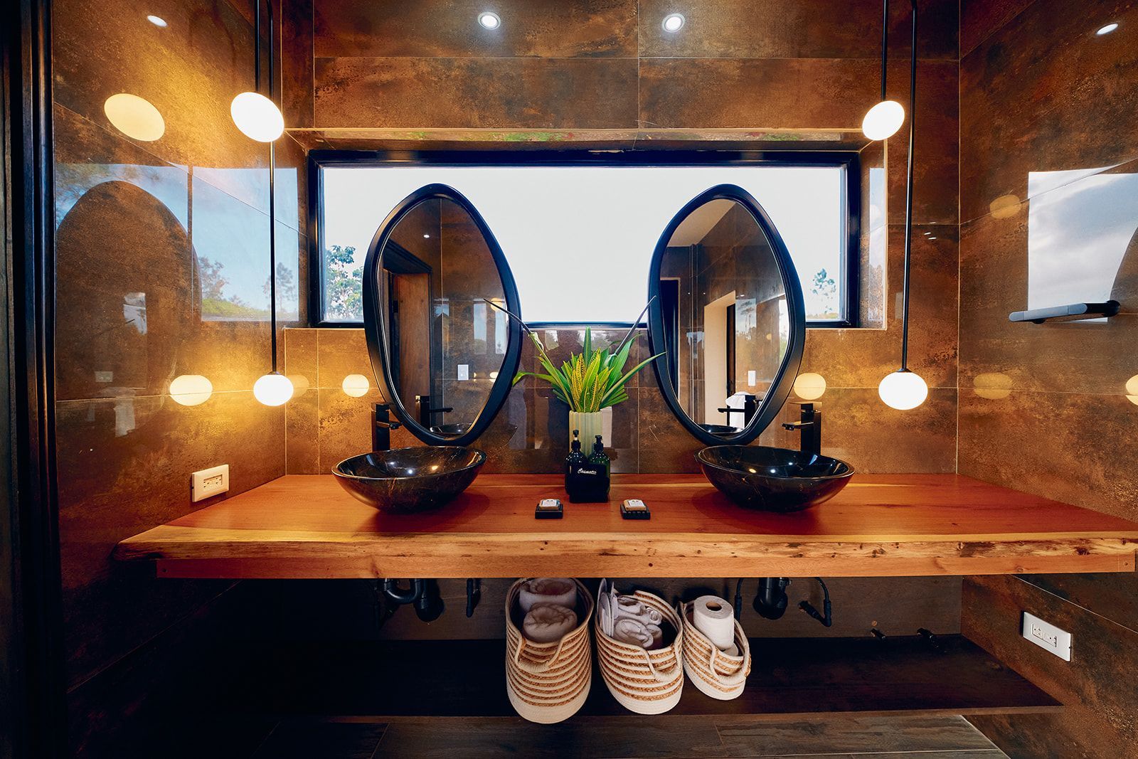 Bathroom with dual sinks, mirrors, and wooden countertop, with hanging pendant lights and a window.