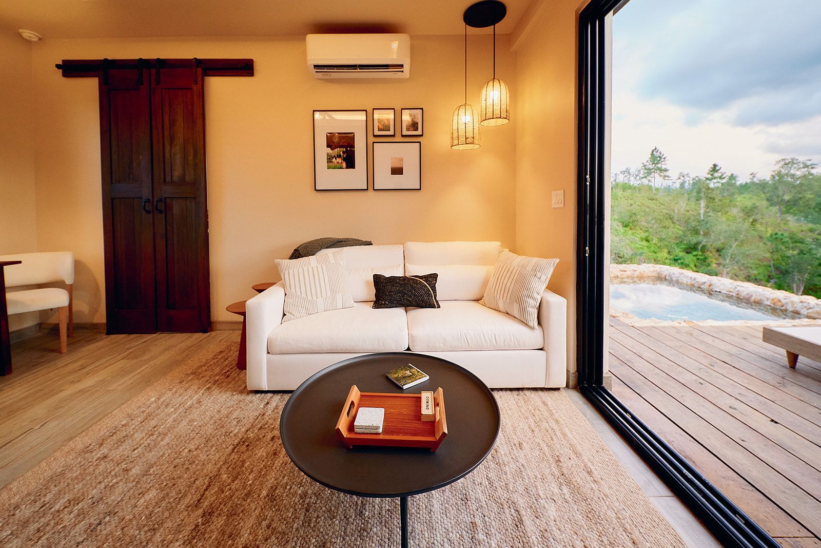 Cozy living room with a white sofa, dark round coffee table, and sliding glass door leading to a deck and pool.