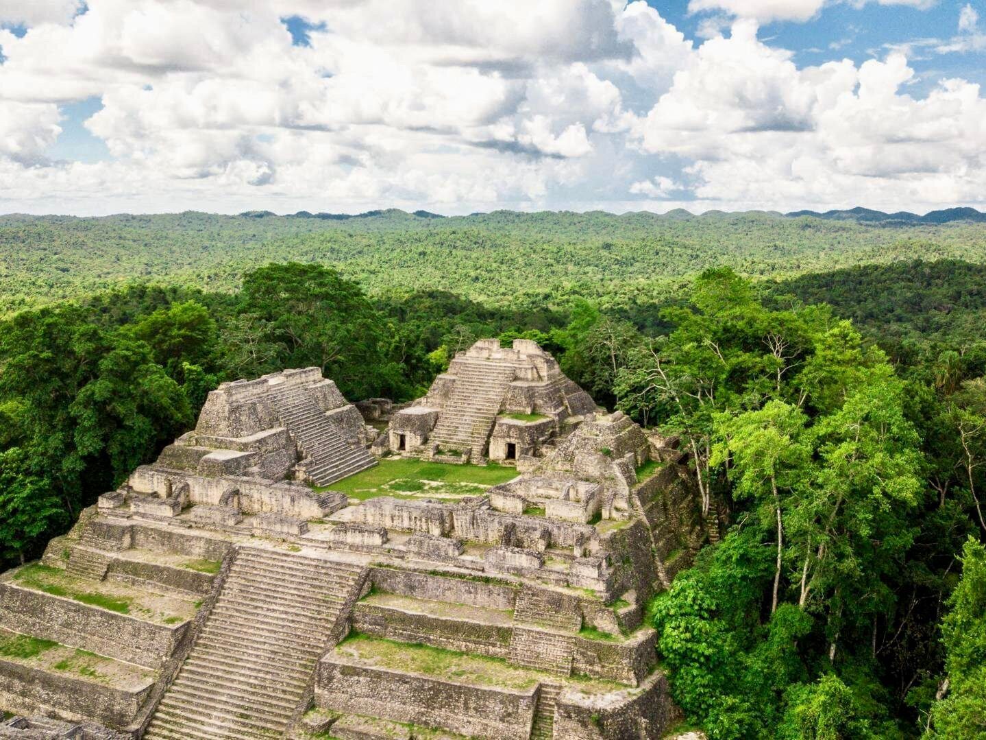 An aerial view of a pyramid in the middle of a lush green forest.