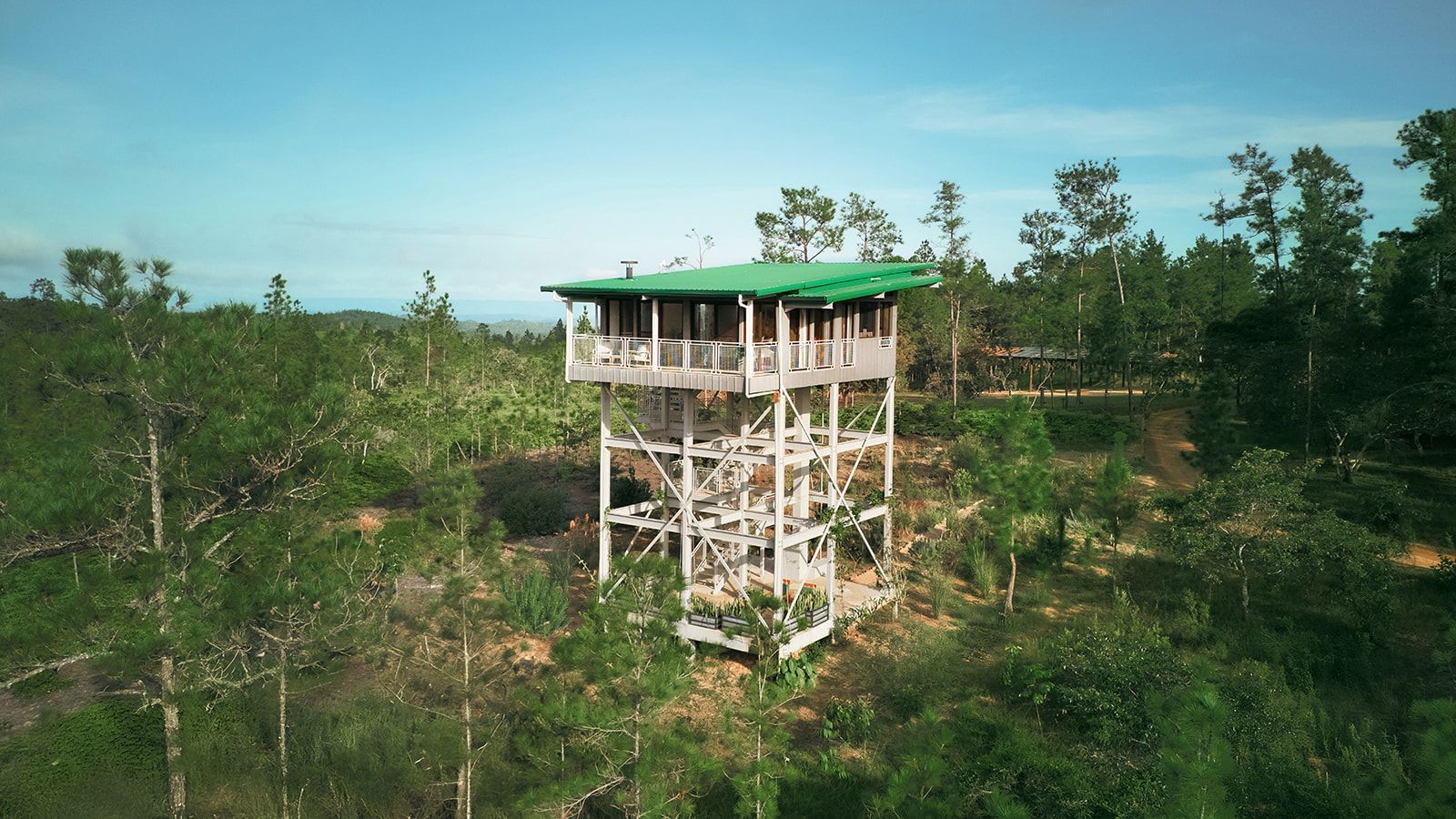 Firetower with a in jungle lodge, set amid lush green trees under a blue sky.