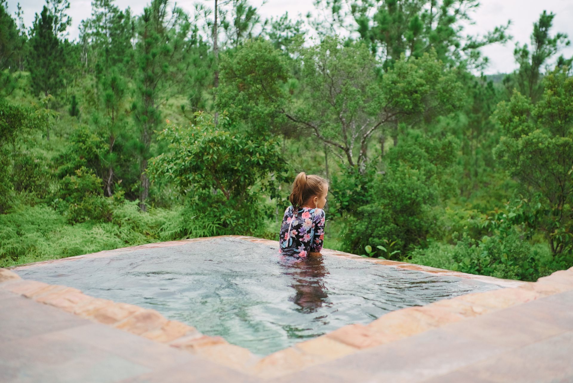 A woman is sitting in a swimming pool surrounded by trees.