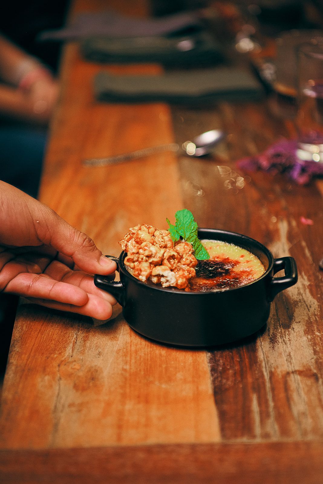 A person is holding a bowl of food on a wooden table.