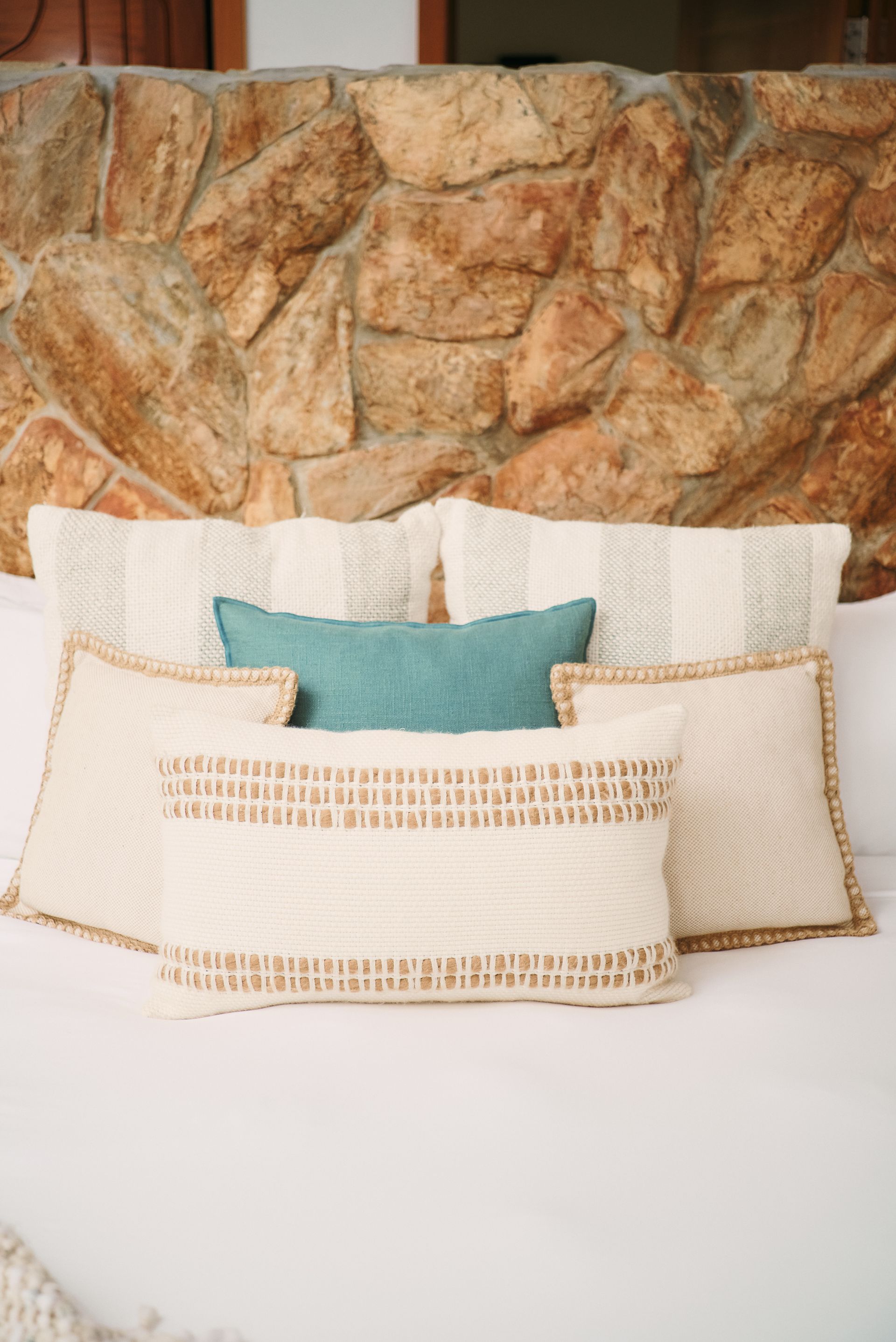 A bed with pillows and a stone wall in the background.