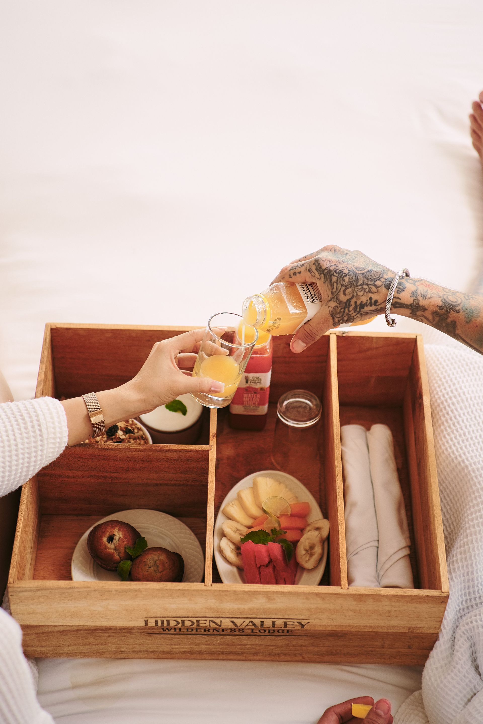 A woman is pouring orange juice into a glass in a wooden box filled with food.