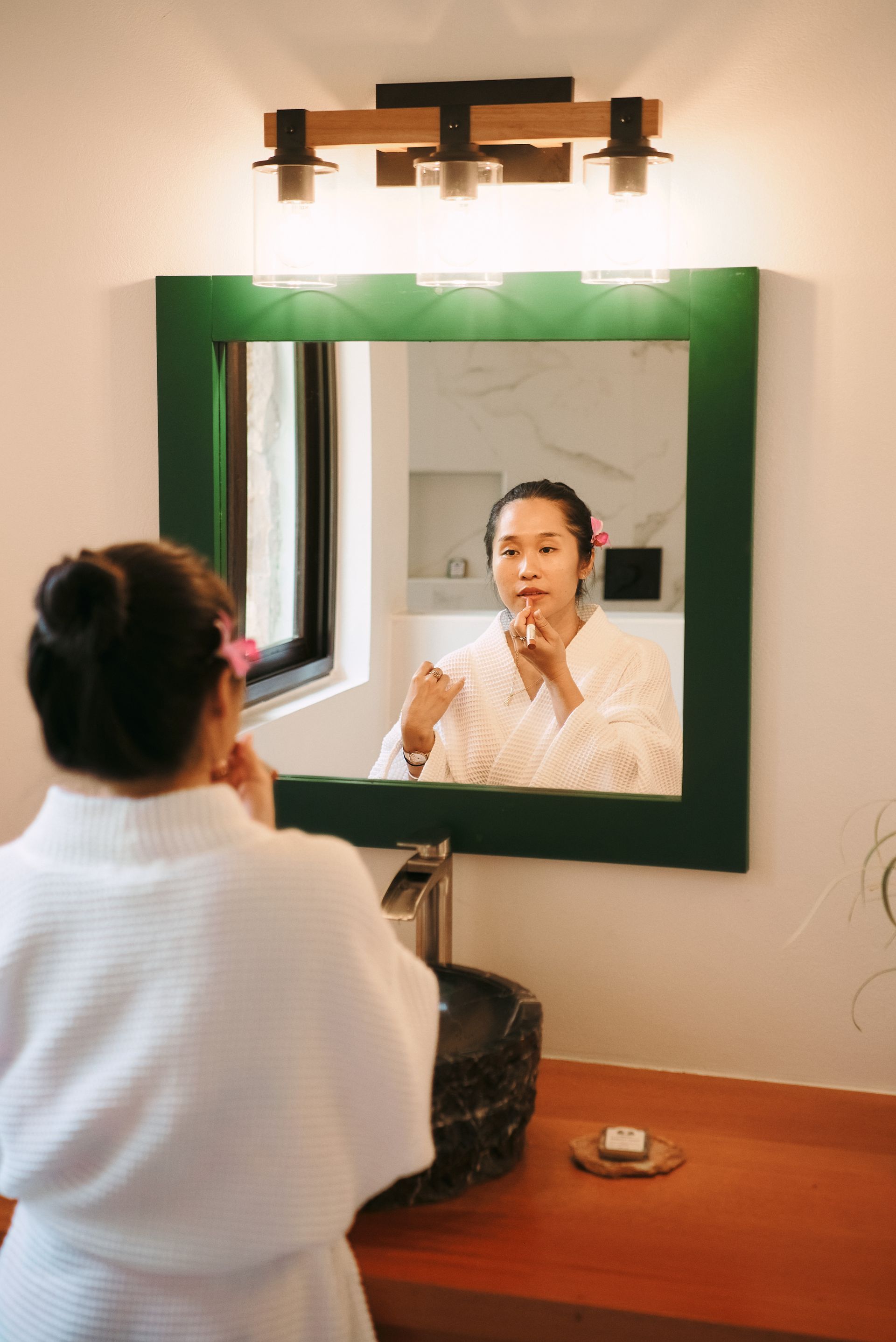 A woman is applying makeup in front of a bathroom mirror.