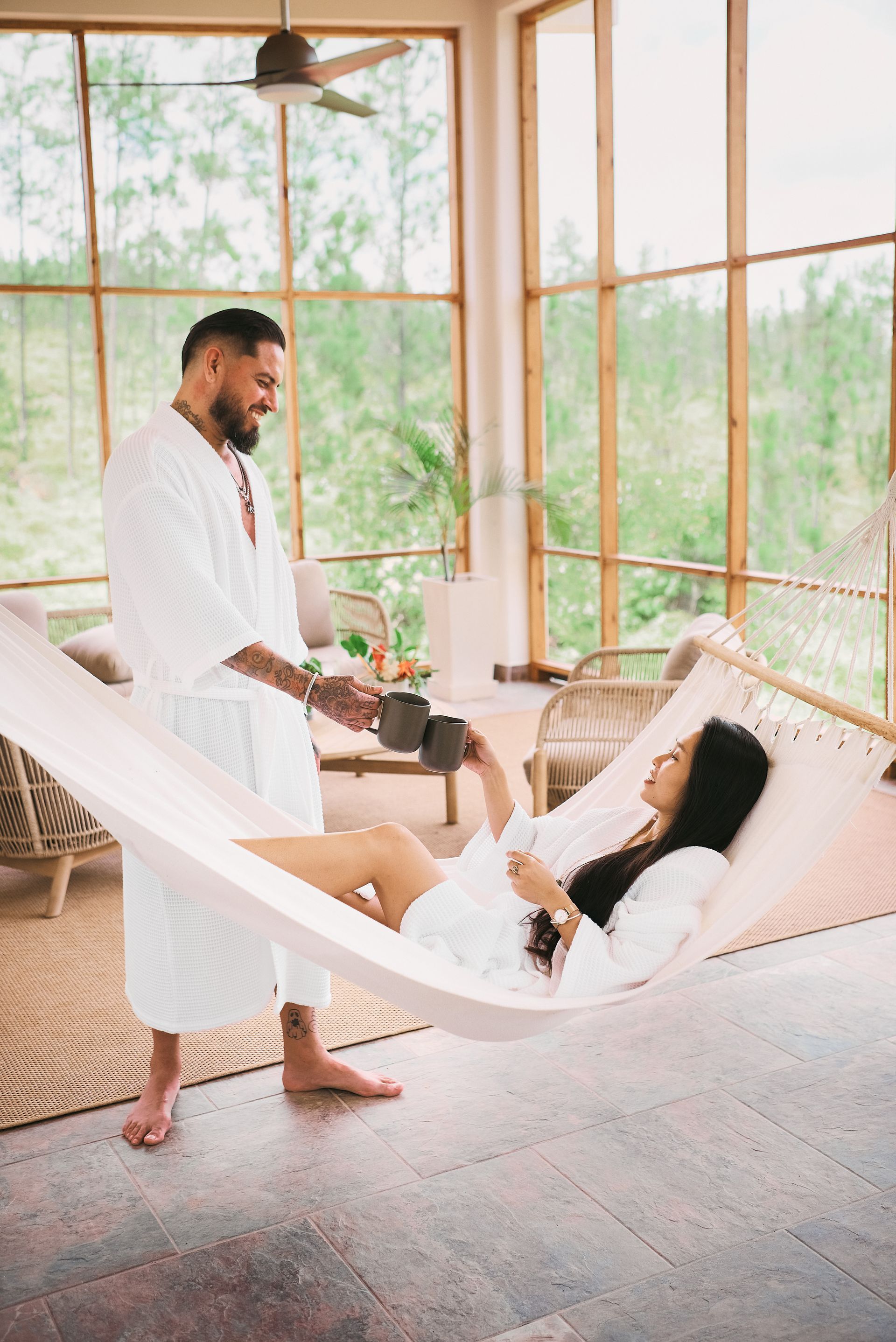 A man is standing next to a woman in a hammock.